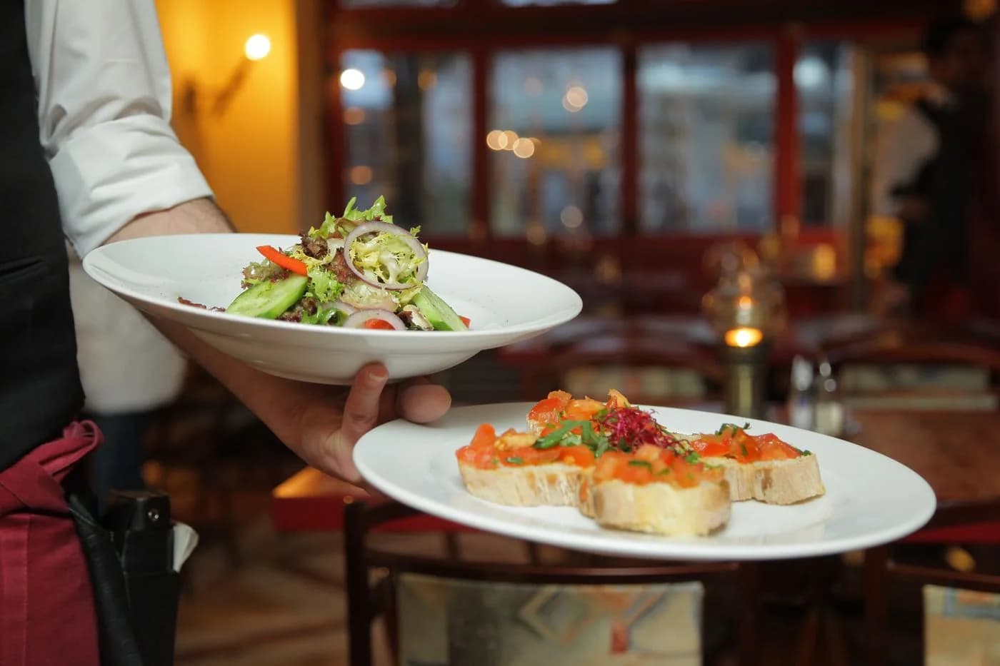 Server carrying plated dishes through a restaurant